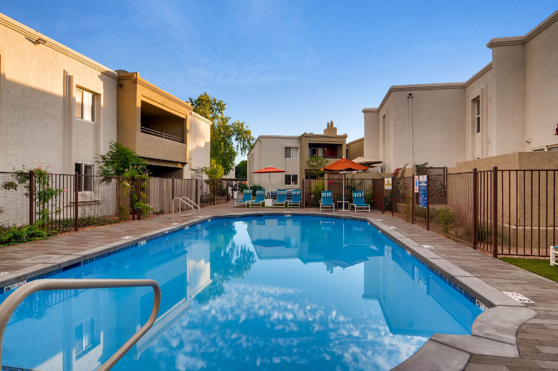 fenced pool with deck seating and umbrellas